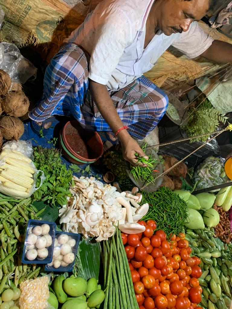 Indian man sitting in front of lots of fruits and vegetables. 